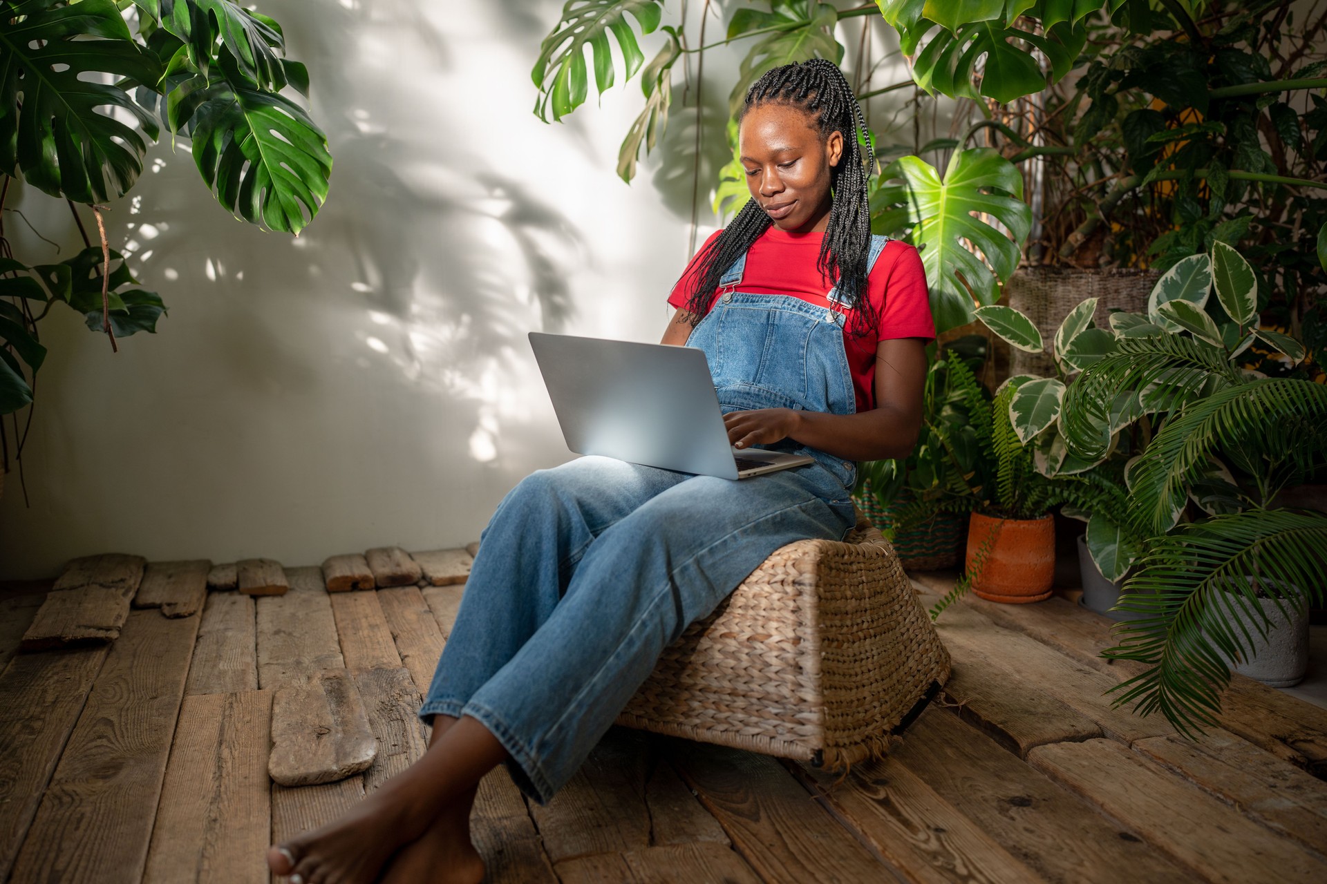 Smiling African American woman using laptop surrounded by plants and flowers. Flower shop owner